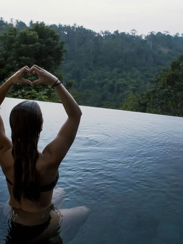 Pessoa relaxando em piscina de borda infinita com vista para a mata